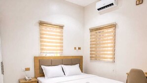 A hotel room with a bed, bedside tables, a desk, and a chair. - The Whale Inn (Kaduna)