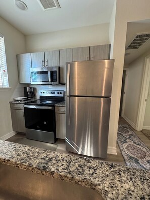 A compact kitchen with stainless steel appliances, including a refrigerator, microwave, and oven. - 1bhk Furnished Retreat Cedar Park Austin Stay (Cedar Park)