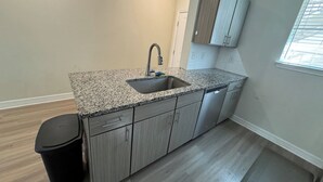 A kitchen with a granite countertop, stainless steel sink, and gray cabinets. - 1bhk Furnished Retreat Cedar Park Austin Stay (Cedar Park)