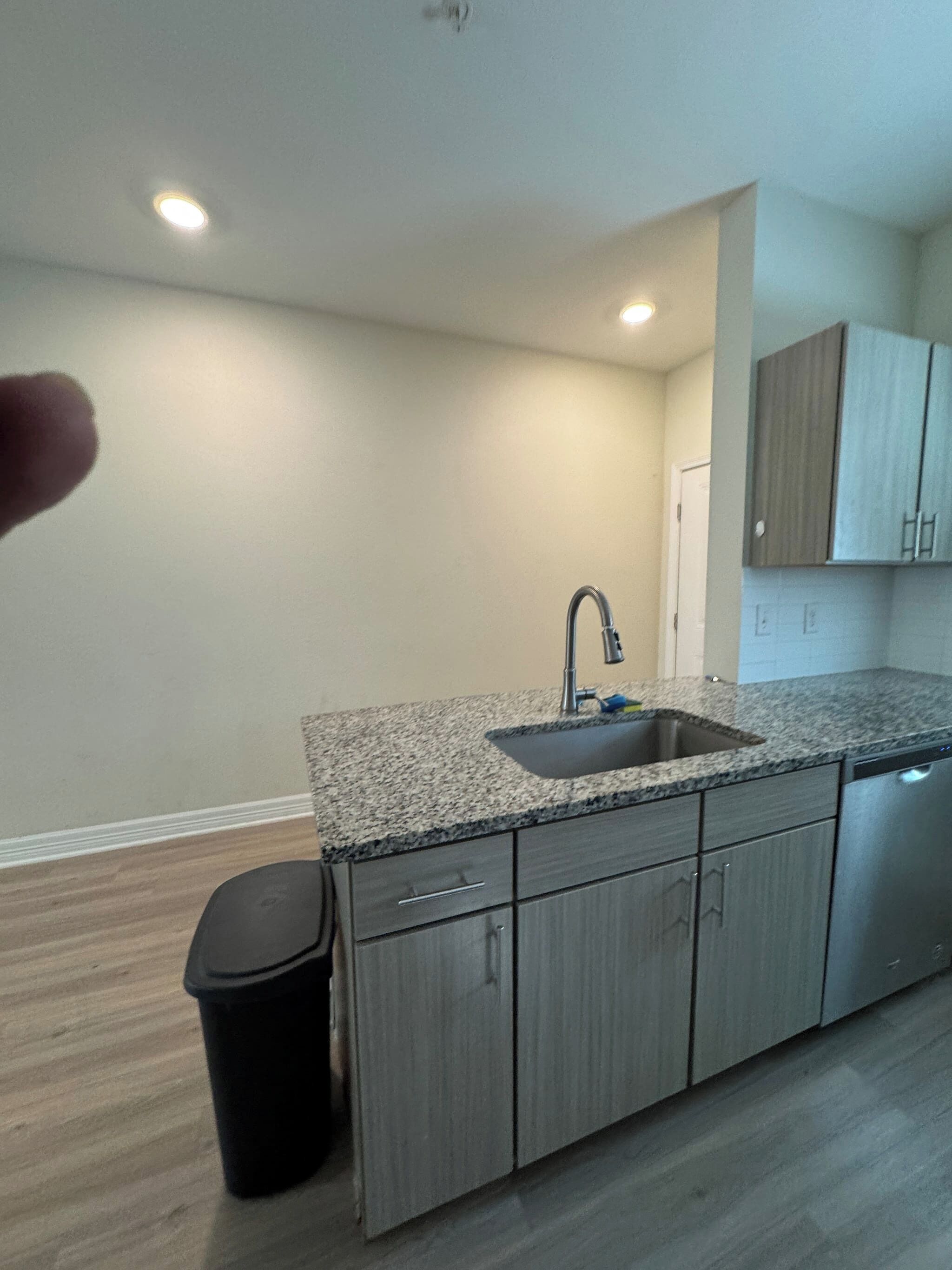 A kitchen with a granite countertop, stainless steel sink, and grey cabinets.