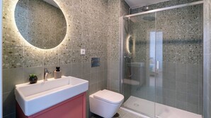 Un baño moderno con un espejo redondo, un lavabo, un inodoro y una ducha con cerramiento de vidrio.