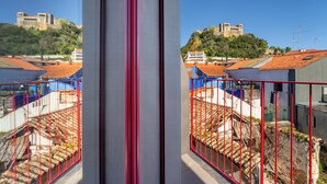 Vista de un castillo histórico sobre una colina, una cerca de metal rojo y edificios con tejados rojos.