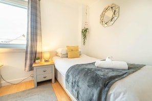 A bedroom with a bed, bedside table, lamp, and a hanging plant. - Highland Holiday Home in Fort William & Ben Nevis | Sleeps 4 (Caol)