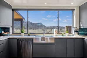 Une cuisine moderne dotée d’une grande fenêtre, de meubles de couleur sombre et offrant une vue sur un paysage montagneux.