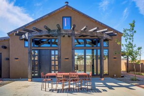 Un bâtiment doté d’une pergola, d’un patio avec une table et des chaises, et de grandes fenêtres.