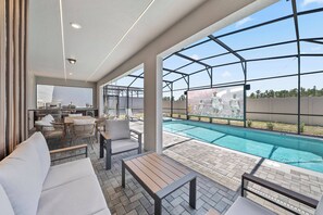 A poolside area with a seating arrangement, a pool, and a view of a sports event. - 10BR house sleeps 26 with private pool (Clermont)