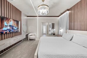 Et moderne hotelværelse med en stor seng, et fjernsyn ophængt på væggen, en lysekrone og et spejl.