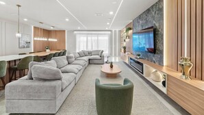 A modern living room with a sectional sofa, a coffee table, and a television mounted on a wooden wall. - 10BR house sleeps 26 with private pool (Clermont)