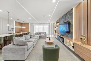 A modern living room with a sectional sofa, a coffee table, and a television mounted on a wooden wall. - 10BR house sleeps 26 with private pool (Clermont)