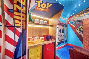 Et livligt legeområde med et 'Toy Story'-tema, med blandt andet et legekøkken, en dinosaurfigur og en rød mikrobølgeovn.