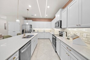 A modern kitchen with white cabinetry, stainless steel appliances, and a tiled backsplash. - 10BR house sleeps 26 with private pool (Clermont)