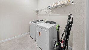 A laundry room with two front-loading washers and dryers, a drying rack, and a vacuum cleaner. - 10BR house sleeps 26 with private pool (Clermont)