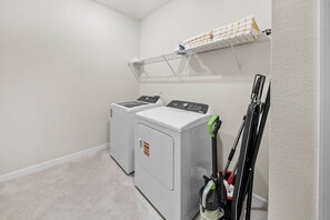 A laundry room with two front-loading washers and dryers, a drying rack, and a vacuum cleaner. - 10BR house sleeps 26 with private pool (Clermont)