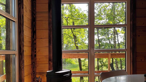Ein Cabin-Interieur mit Kaminofen, Esstisch mit Stühlen und großen Fenstern mit Blick auf Bäume.