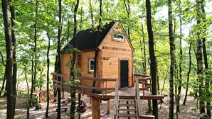 Eine Holzhütte mit kleinem Fenster und Tür, umgeben von Bäumen.