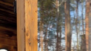 Interno di una baita di legno con lavandino a vista e finestra su una zona boschiva.