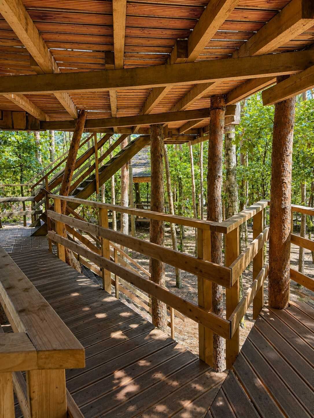 A wooden deck with railings, supported by natural tree trunks, in a forested area.