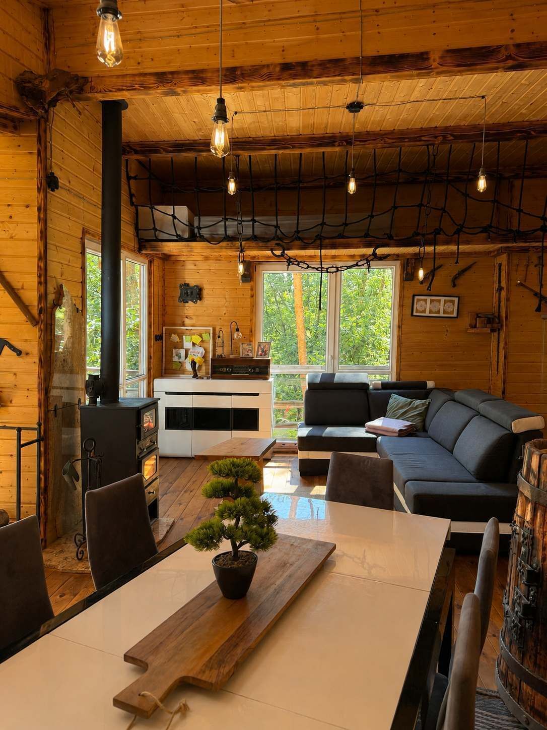 Interior acolhedor de uma cabana, com decoração em madeira, lareira, área de jantar e sofá.