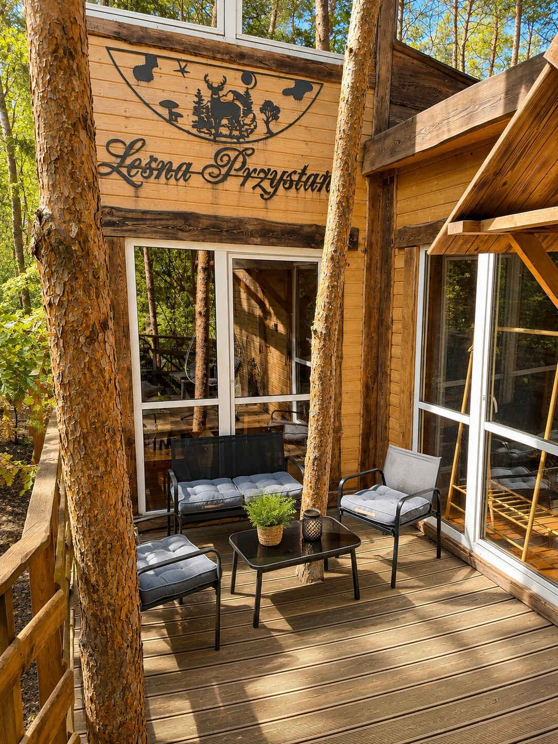 Une cabane en bois avec une terrasse, un canapé et une table agrémentée d’une plante.