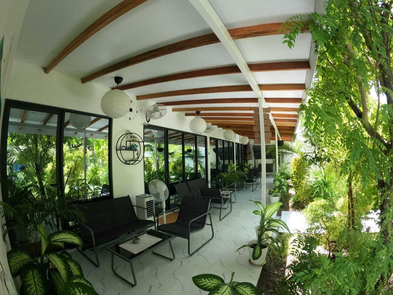 An indoor space with a ceiling supported by wooden beams, large windows, and indoor plants.