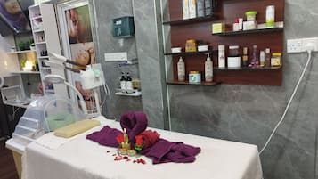 Un cuarto de tratamientos de spa con una camilla de masaje, un estante empotrado con diversos productos para el cuidado de la piel y un cartel en la pared.