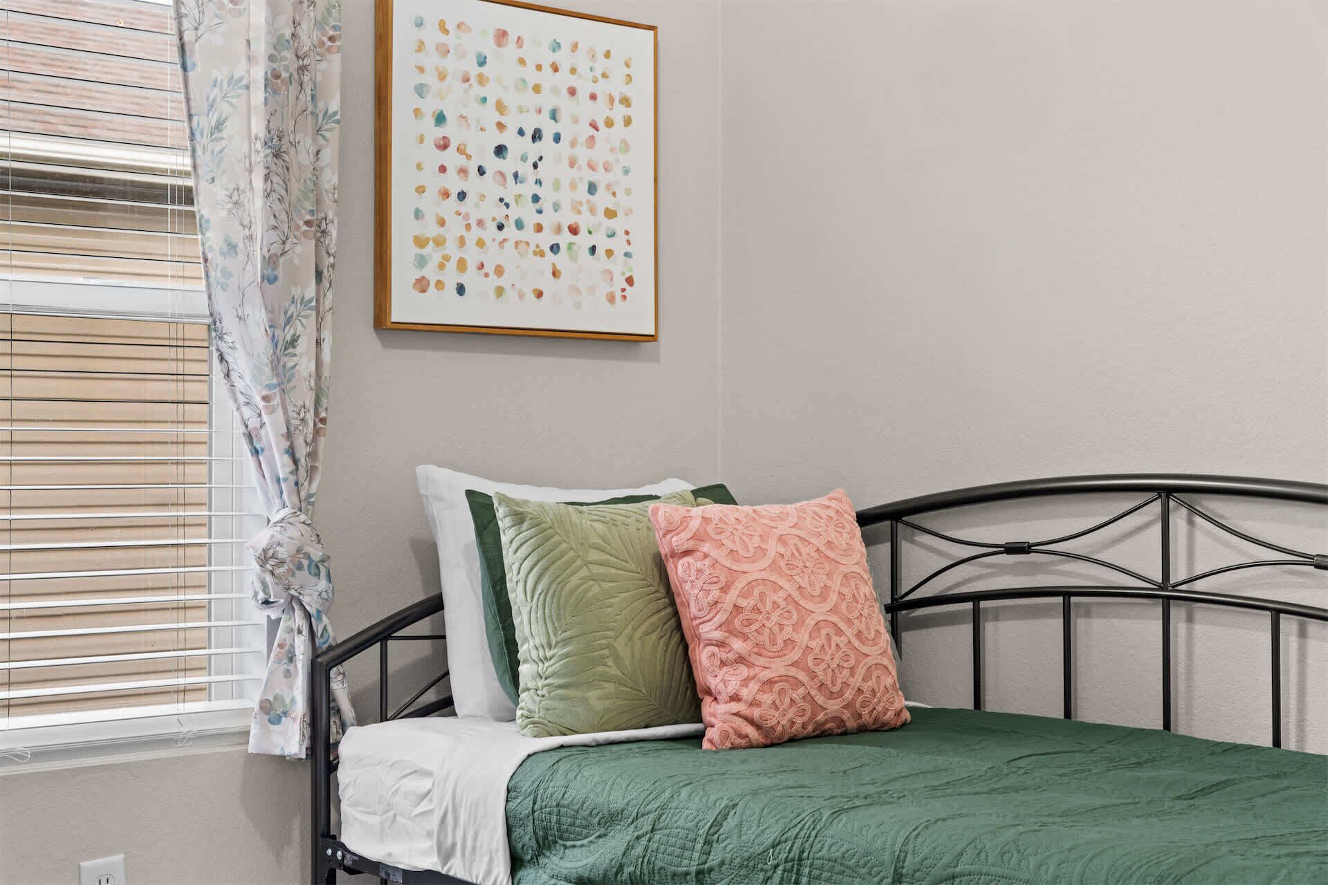 Uma cama com colcha verde, travesseiro branco e travesseiro rosa com estampas florais.