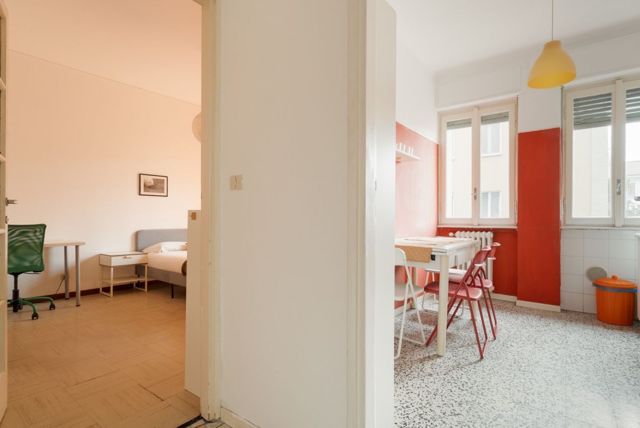 A room with a bed, a desk, a chair, a window with blinds, and a door.