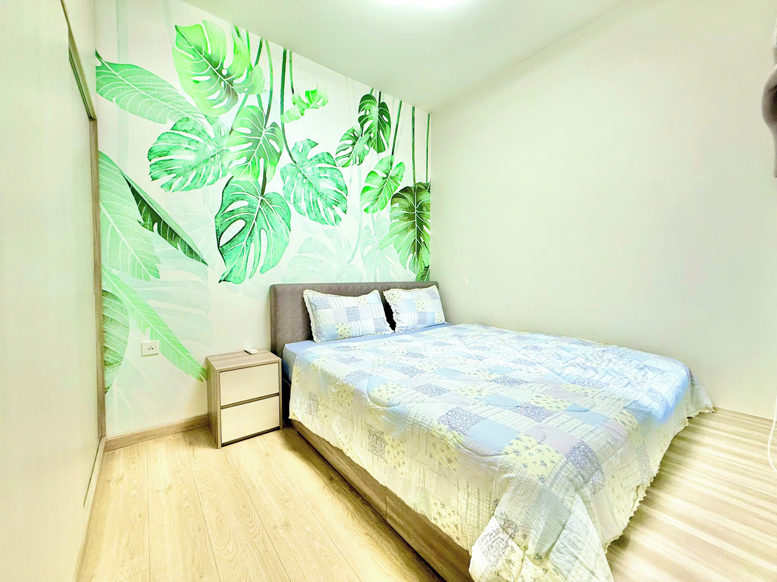A bedroom with a bed, a nightstand, and a wall with a tropical leaf mural.