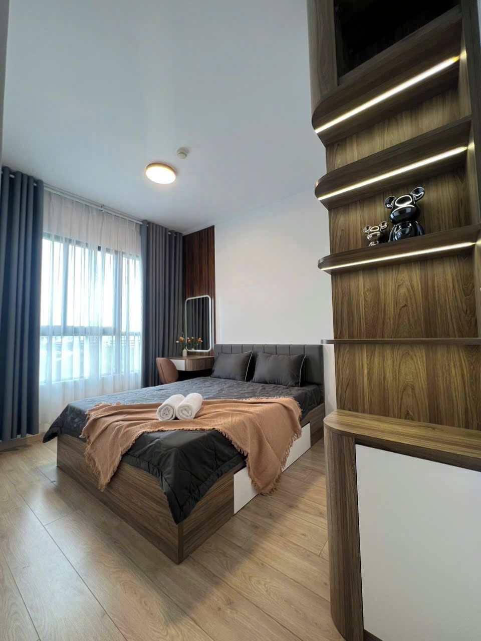 Un dormitorio moderno con una cama grande, una mesita de noche, un espejo y un estante empotrado con adornos decorativos.