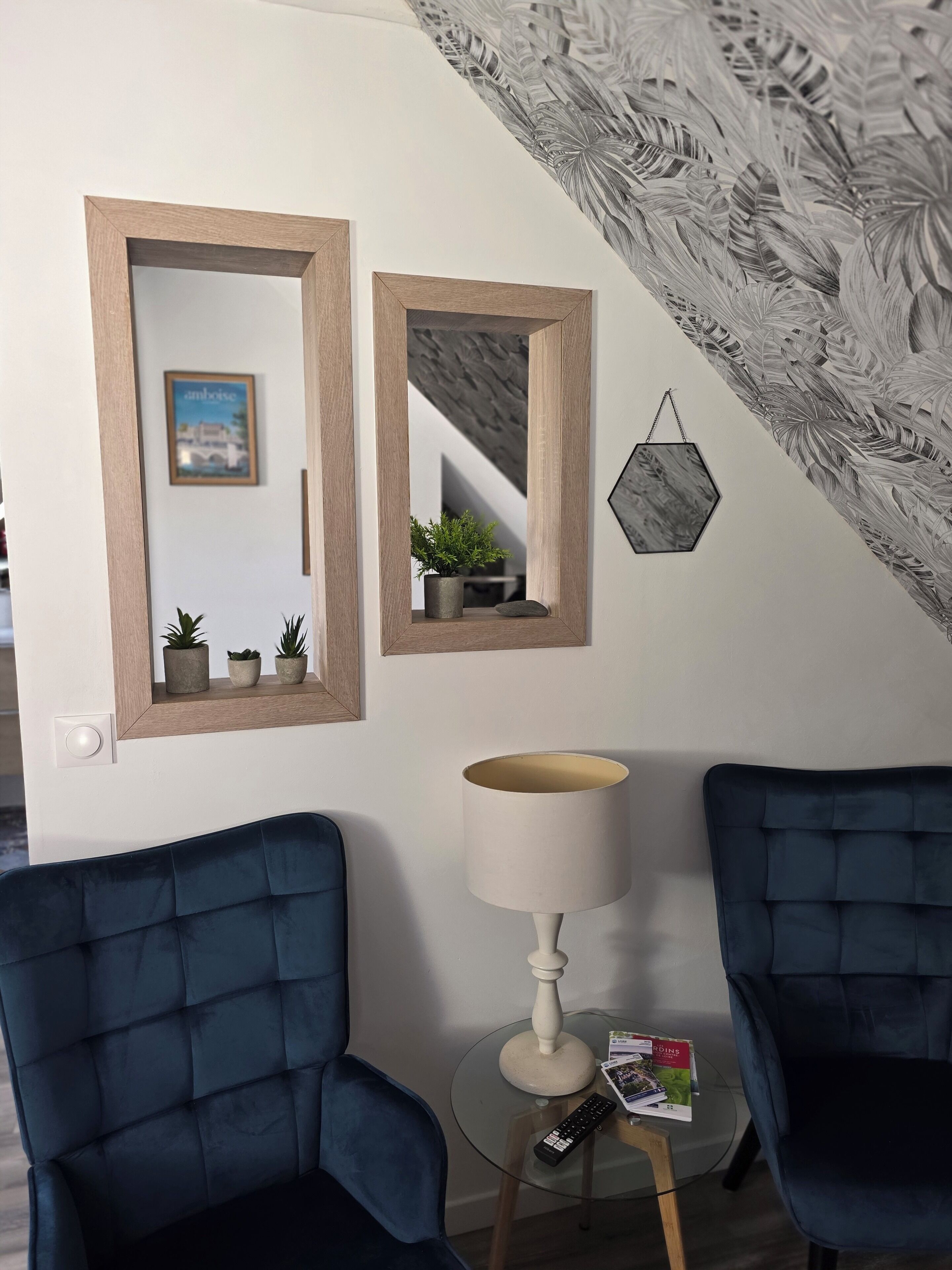 A room with two blue chairs, a lamp, a small table with a remote control, and a framed picture on the wall.