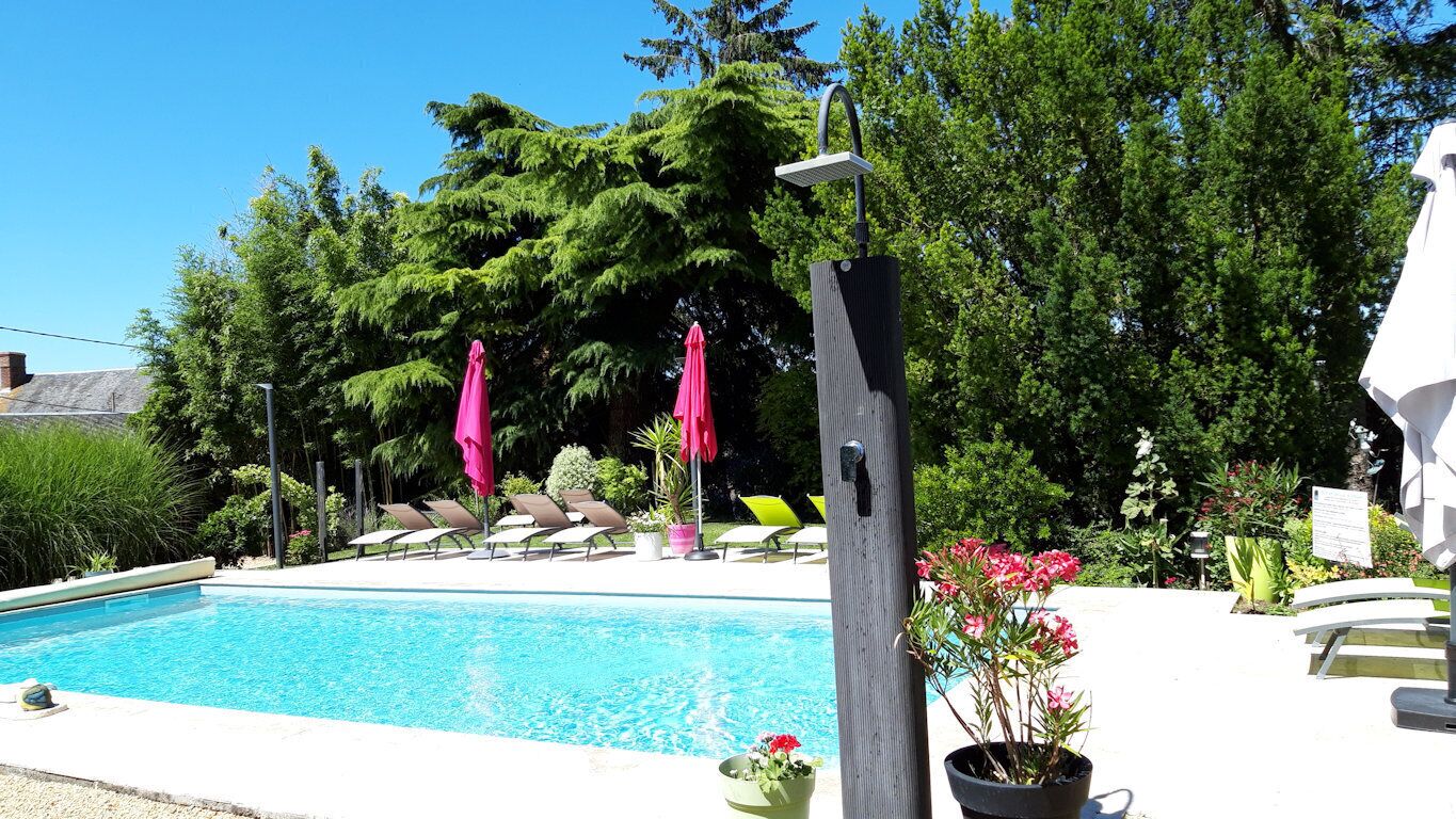 A swimming pool with lounge chairs and umbrellas, surrounded by greenery and a building.