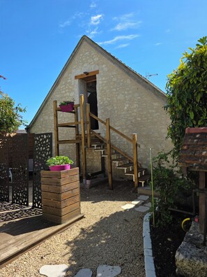 A stone building with a wooden staircase leading to a door, surrounded by gravel and plants. - GITE L'Essentiel Piscine clim between Beauval Futuroscope and Châteaux de la Loire (Sainte-Maure-de-Touraine)