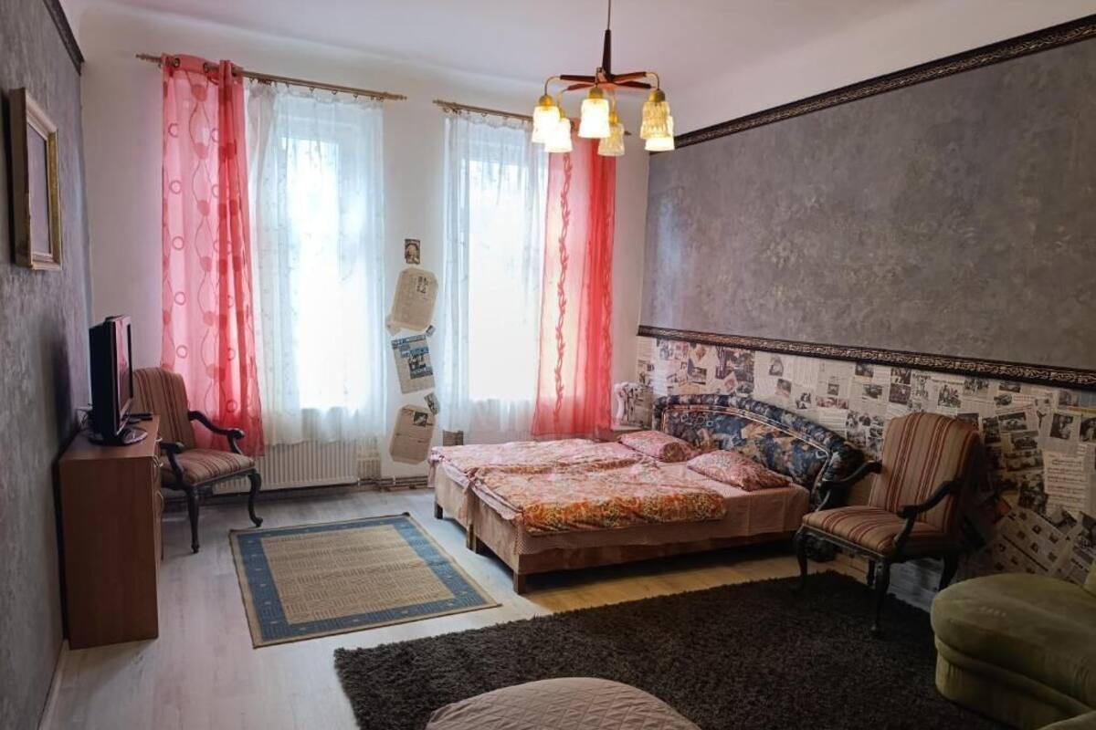 A bedroom with a bed, two chairs, a radiator, and a window with curtains.