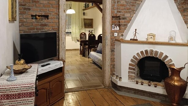 Una sala de estar con chimenea de ladrillo, un televisor y un comedor visible a través de un arco.