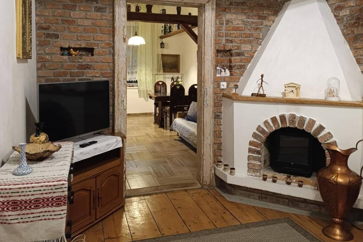 A living room with a brick fireplace, a television, and a dining area visible through an open doorway.