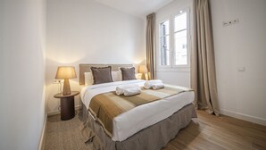 Un lit bien fait, recouvert d’une couverture à rayures, avec deux lampes de chevet et une fenêtre avec des rideaux.