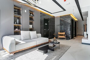 Uma sala de estar moderna com um sofá cinzento, uma mesa de centro preta e uma porta de vidro que dá para outro espaço.