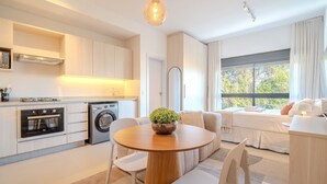 Une cuisine moderne dotée d’appareils électroménagers intégrés, un coin repas avec une table ronde en bois et une grande fenêtre donnant sur les arbres.