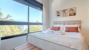 Une chambre d’hôtel moderne avec une grande fenêtre, un lit soigneusement fait et des œuvres d’art accrochées au mur.