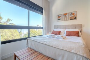Quarto de hotel moderno com uma grande janela, uma cama bem arrumada e obras de arte na parede.
