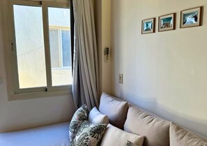Ein Zimmer mit einem Bett, einem Vorhangfenster, einem an der Wand befestigten Telefon und drei gerahmten Bildern.