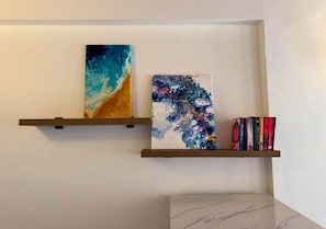 Two wall-mounted shelves with abstract paintings and books.