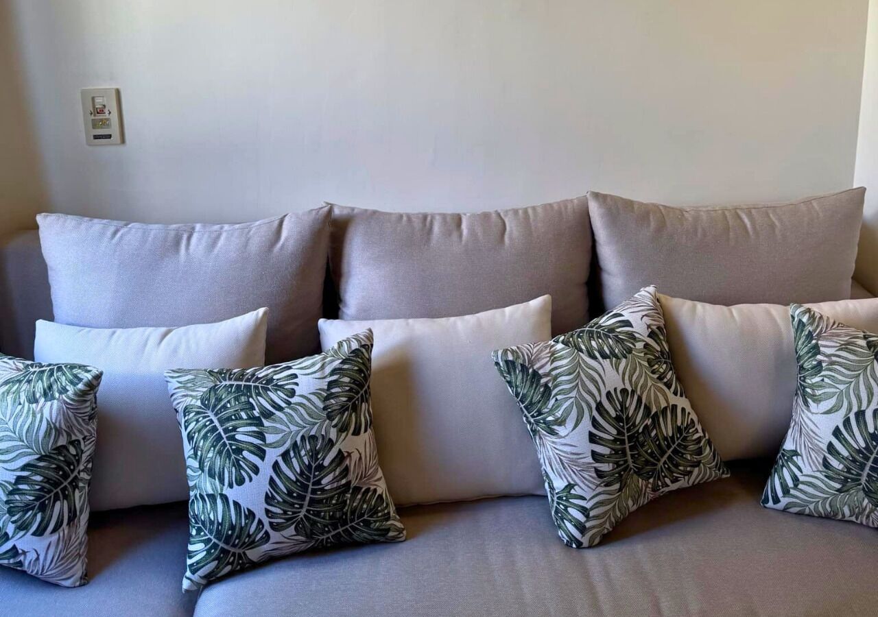 A sofa with multiple cushions, some plain and some with a leaf pattern.