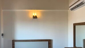 Hotellihuone, jossa on sänky, seinään kiinnitetty valaisin ja ilmastointilaite.