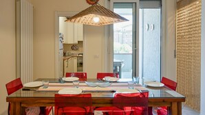 A dining area with a glass table, red chairs, a woven pendant light, and a view through a glass door. - Comfortable 75 sqm apartment, accommodating up to 6 people, located on the second floor of a building without an elevator.The property is located in Luni Mare, in a well-served residential area. The location is convenient, a short distance from the sea a (Luni)