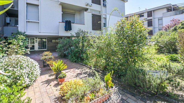 A multi-story residential building with a courtyard garden, balconies, and a visible entrance. - Comfortable 75 sqm apartment, accommodating up to 6 people, located on the second floor of a building without an elevator.The property is located in Luni Mare, in a well-served residential area. The location is convenient, a short distance from the sea a (Luni)