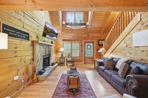 A log cabin interior with a fireplace, a sofa, a rug, and a sign on the wall. - Be Still | MTN Views, Hot Tub, Grill, Fireplace! (Sevierville)