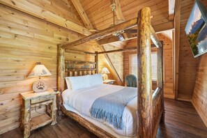 A wooden four-poster bed with a headboard, a nightstand with a lamp, and a chair in a log cabin room. - Be Still | MTN Views, Hot Tub, Grill, Fireplace! (Sevierville)