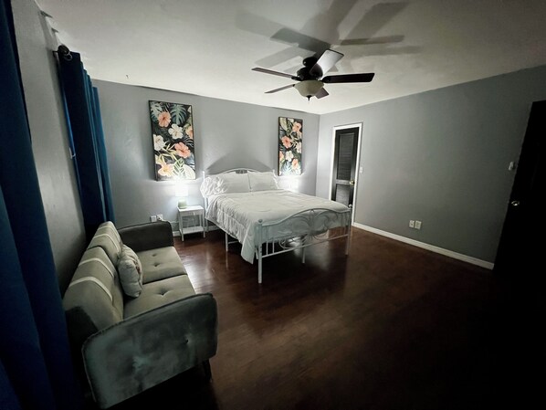 A bedroom with a bed, a ceiling fan, a nightstand, and a couch.