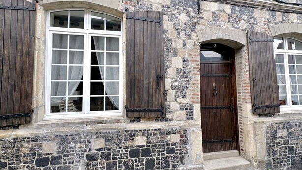 Un bâtiment en pierre doté d’une grande fenêtre en arc de cercle, d’une porte en bois et de fenêtres fermées par des volets.